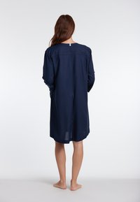 Abito blu navy a maniche lunghe con vestibilità ampia, scollatura rotonda e dettaglio di cucitura sul retro. Tessuto morbido e design lungo fino al ginocchio.