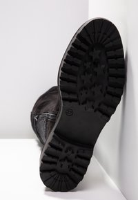 Schwarze Wildlederboots mit einer strukturierten Gummisohle, die ein Sternmuster aufweist. Ein seitlicher Reißverschluss ist sichtbar, und Größe 37 ist auf der Sohle markiert.