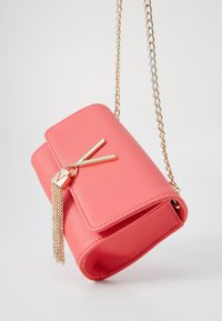 Korallinpunainen käsilaukku, jossa on teksturoitu pinta, kultaiset yksityiskohdat, ketjuhuoma ja näyttävä kultainen tupsukoriste. Suorakulmainen muoto.