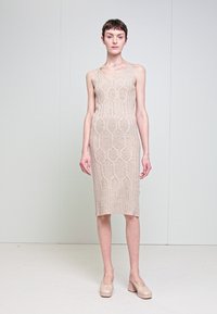 Abito lavorato a maglia beige con silhouette aderente, caratterizzato da un motivo geometrico e una texture a costine. Indossato con tacchi di colore chiaro.