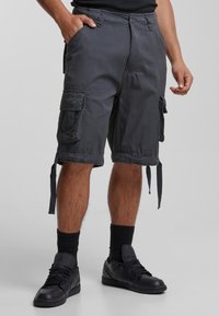 Shorts cargo en tissu gris foncé avec poches latérales, liens ajustables au bas, et coupe décontractée. Portés avec des baskets noires et des chaussettes.