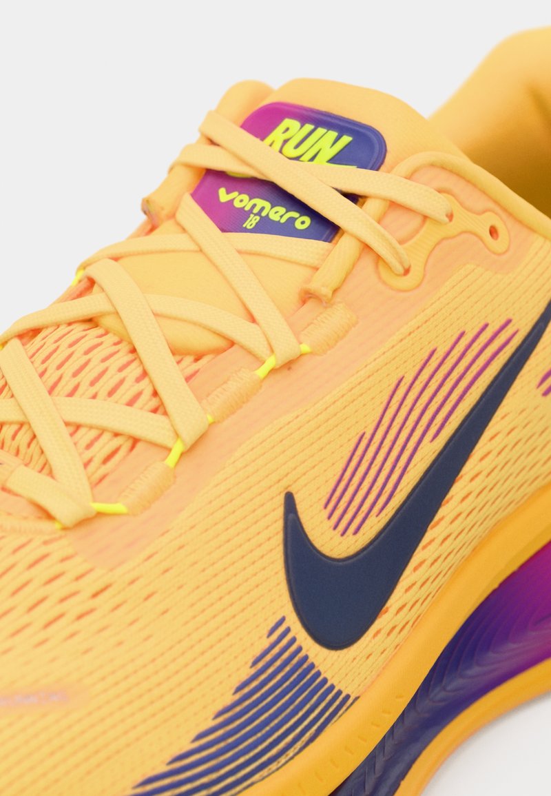 Zapatilla de running Nike Vomero 18 en vibrante naranja con detalles en púrpura, cuenta con una parte superior de malla texturizada, lengüeta acolchada y cordones amarillos.