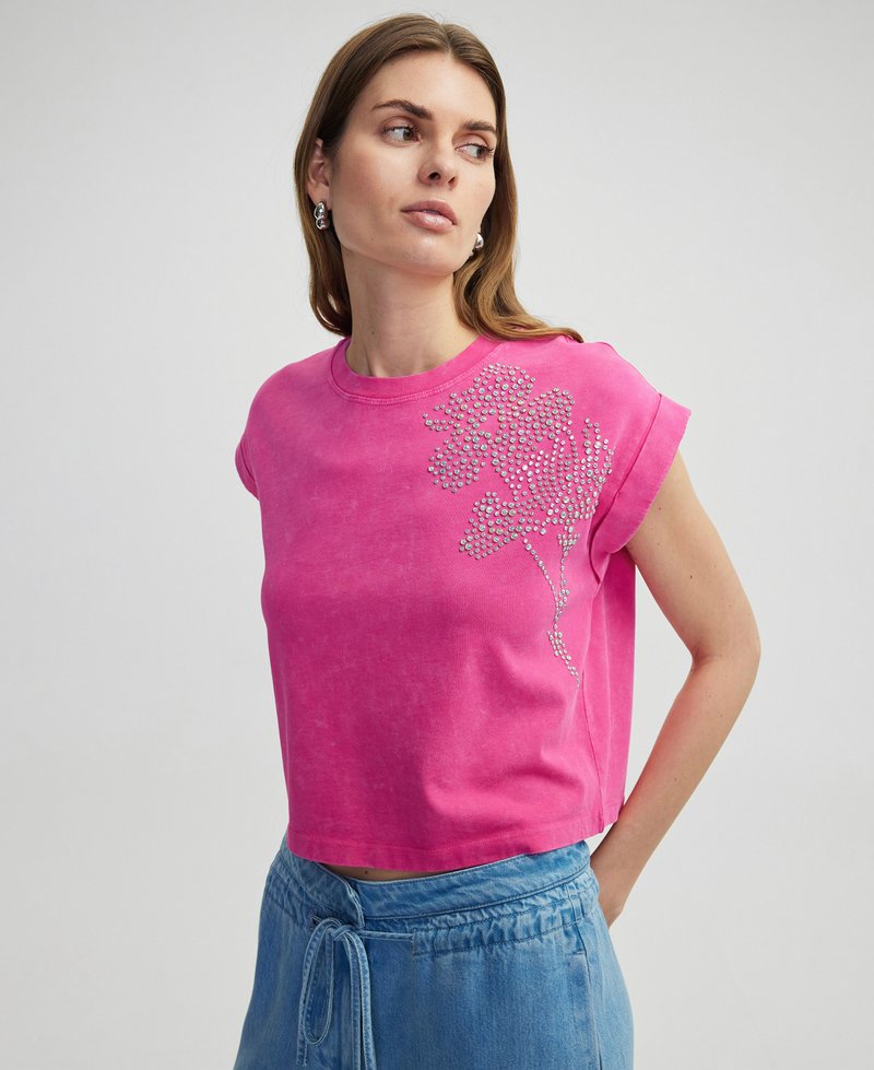 Różowy krótki t-shirt z krótkimi rękawami, zdobiony kwiatowym wzorem wykonanym z błyszczących cyrkoni na lewej stronie. Miękka tekstura materiału.