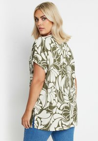 Top a maniche corte in verde oliva con motivo floreale bianco, texture a costine, spacchi laterali e vestibilità rilassata. Adatto per un abbigliamento casual.