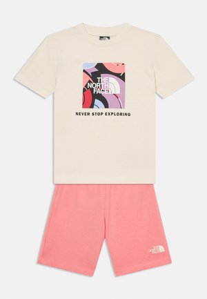 Beež lühikeste varrukatega t-särk mitmevärvilise abstraktse logoga ja tekstiga "THE NORTH FACE NEVER STOP EXPLORING", mida kannavad roosad lühikesed püksid.