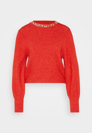 Rød striktrøje med rund halsudskæring, der har en perlekant. Lange ærmer med ribbede manchetter og en cropped længde. Blød tekstur.