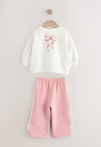 Sweat-shirt blanc à manches longues pour tout-petit avec un motif de nœud rose, associé à un pantalon rose à taille élastique avec des bandes de dentelle blanche et de petits nœuds.