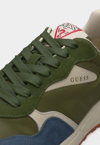 Πράσινο, μπεζ και μπλε αθλητικό παπούτσι Guess με πράσινα κορδόνια και λογότυπο της μάρκας στο πλάι και τη γλώσσα, κοντινή λήψη.