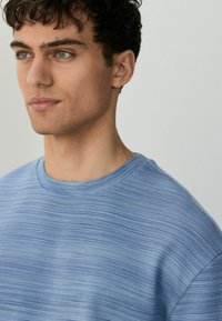 Lys blå tekstureret t-shirt med rund hals. Har et diskret stribet mønster og korte ærmer. Glat stof med en afslappet pasform.