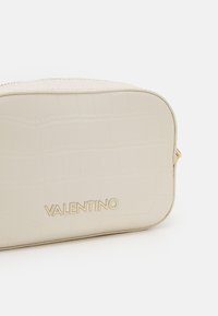 Kremowa kosmetyczka z ekoskóry o fakturze krokodyla, zaokrąglone krawędzie i złote akcesoria z wytłoczonym na przodzie logo "VALENTINO".