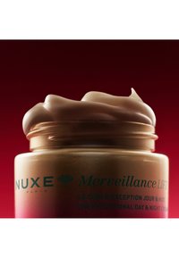 Barattolo di vetro dorato con coperchio color crema, riempito con una crema leggera e densa. L'etichetta presenta testo verde su uno sfondo rosso sfumato.