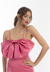 Rochie roz din satin cu un detaliu mare sub formă de fundă la bust, bretele subțiri, fustă ajustată și textură netedă.