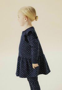 Marineblauwe jurk met lange mouwen met een print van witte, roze en rode harten, voorzien van gerimpelde mouwen en een uitlopende zoom. Gecombineerd met bijpassende legging.