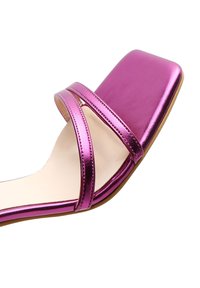 Sandale à bout ouvert avec des brides métalliques roses et un bout carré sur une semelle beige clair à semelle plate marron.