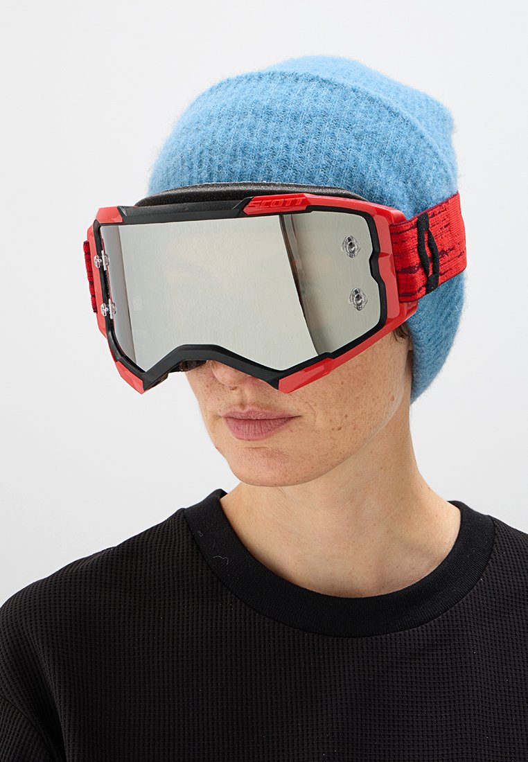 Person trägt eine hellblaue Strickmütze und große rote Skibrillen mit reflektierenden Gläsern, bekleidet mit einem schwarzen, strukturierten Oberteil.