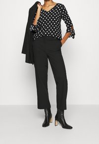 Sorte og hvide polkaprikker top med V-hals, parret med sorte bukser og ankelstøvler. Outfittet er suppleret med en sort blazer.