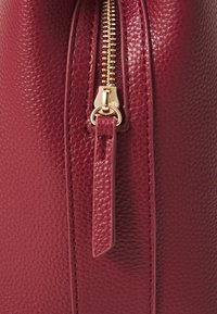Sac à main en cuir bordeaux avec une finition texturée, présentant une fermeture éclair dorée et un détail de tirette sur un côté.