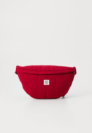 Rote gesteppte Tasche mit geschwungener Form, ausgestattet mit einem Reißverschluss und einem kleinen Logopatch auf der Vorderseite. Glatte Textur und weiches Material.