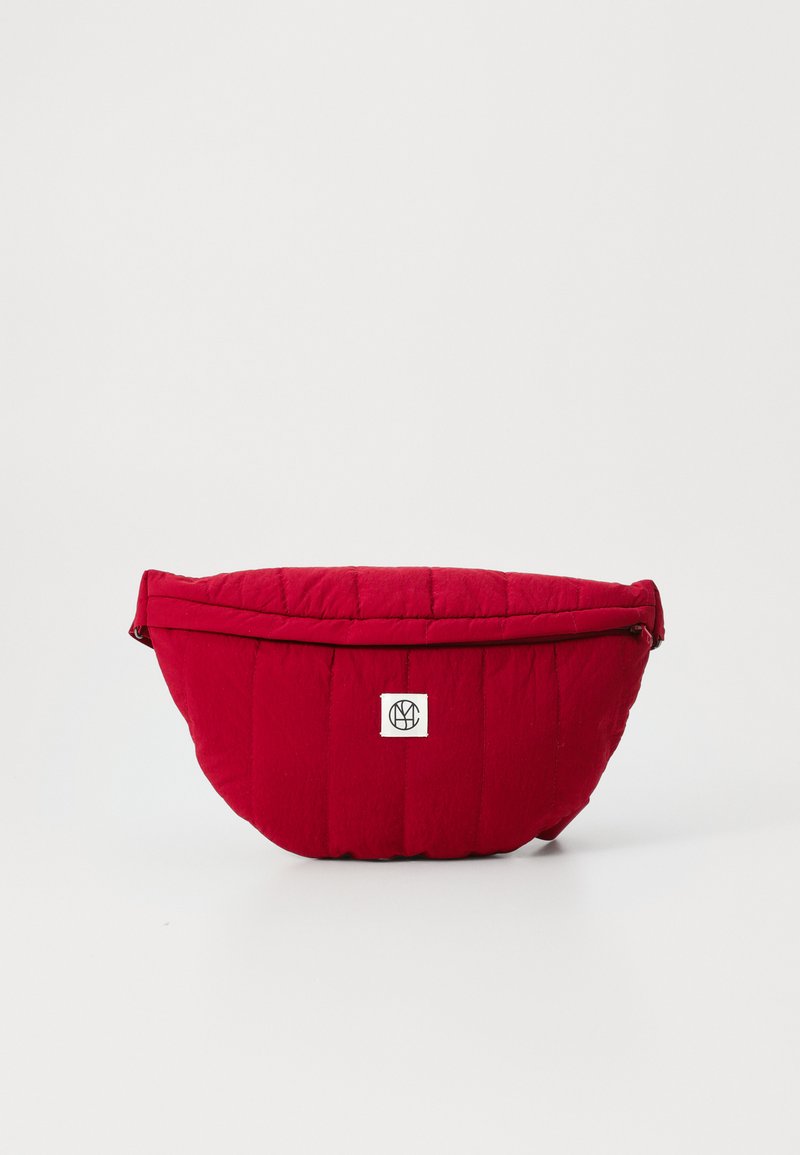 Borsa trapuntata rossa con una forma curvilinea, dotata di chiusura a zip e di una piccola etichetta con logo sul davanti. Texture liscia e materiale morbido.