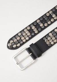 Ceinture en cuir noir ornée de clous texturés argentés et gris disposés en motif circulaire, avec une boucle en métal rectangulaire et plusieurs trous de réglage.