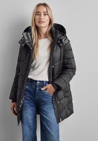 Svart puffjacka med huva, med en kviltad design och glänsande detaljer. Kombinerad med ljusblå vida jeans och en beige topp.