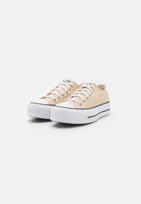 Baskets basses en toile beige avec semelles en caoutchouc blanc, accents de rayures noires et lacets blancs. Dotées d'un bout rond et de détails à œillets.