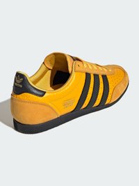 Gelbe Ledersneaker mit schwarzen Wildlederakzenten, drei schwarzen Streifen, strukturiertem Sohlen und geprägtem Logo an der Ferse.