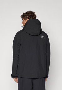 Veste à capuche noire avec une texture lisse, présentant un logo dans le dos, des poignets élastiques et un ourlet droit. Design minimaliste.
