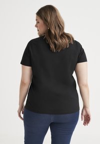 Zwarte T-shirt met korte mouwen, gemaakt van zachte stof, met een ronde halslijn en eenvoudig ontwerp. Draagt met donkerblauwe jeans.