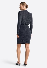 Vestido negro de manga larga con tela texturizada y brillante. Diseño ajustado con detalles fruncidos en la cintura y una longitud a medio muslo.