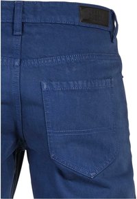 Un jean en denim bleu présente une poche arrière avec des coutures discrètes, une étiquette en cuir au niveau de la taille et un design à jambes droites.