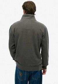 Grijs fleece sweatshirt met een hoge kraag en een vierkante patch op de bovenrug. Voorzien van geribbelde manchetten en een afgeronde zoom.