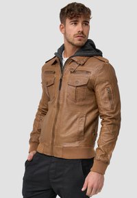 Veste en cuir marron avec une fermeture éclair à l'avant, deux poches poitrine, des poignets côtelés et un sweat à capuche gris superposé en dessous.