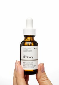 Bouteille en verre ambre avec un bouchon compte-gouttes blanc ; étiquetée "The Ordinary" avec les détails du produit en texte noir, présentant un design épuré et clinique.
