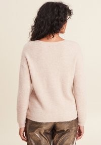 Lichtroze gebreide trui met een relaxte pasvorm, geribbelde textuur en een wijde halslijn, gecombineerd met glanzende metallic gouden broek.