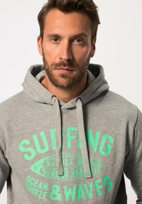 Felpa grigia in cotone con una grafica frontale in testo verde che leggono "SURFING OCEAN BREEZE & WAVES." Presenta lacci e una vestibilità comoda.