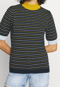 Stickad kortärmad topp med marinblå, gul och vit randning, med en gul hälsguide och ljusblå detaljer på ärmarna.