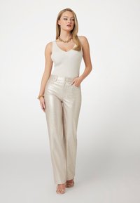 Pantalones anchos metálicos plateados con una textura suave, combinados con una camiseta sin mangas de punto crema y un collar grueso dorado.