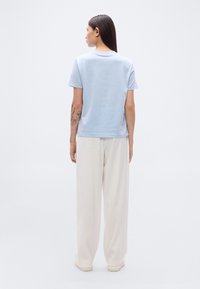 Φωτεινό γαλάζιο βαμβακερό t-shirt με κοντά μανίκια και στρογγυλή λαιμόκοψη, συνδυασμένο με λευκό παντελόνι φαρδιάς γραμμής. Λεία υφή, μινιμαλιστικός σχεδιασμός.