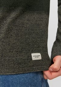 Sötétzöld kötött pulóver, texturált mintával. Anyagcímkéje "JACK & JONES EST. 1990" felirattal. Az ujjak és az alja bordás szabású.