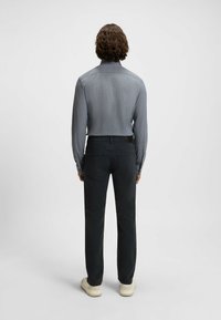 Camisa gris de mangas largas con cuello, combinada con pantalones oscuros y zapatillas de color claro. Tejido suave; diseño minimalista sin patrones.