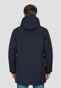 Veste matelassée bleu marine avec capuche. Présente une coupe droite et des manches longues, fabriquée en tissu texturé et résistant à l'eau.
