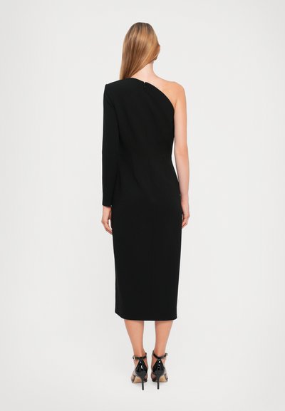 Crna midi haljina s jednim dugim rukavom i jednim golim ramenom, sa uskim siluetom i zatvaranjem na patentni zatvarač na leđima. Crne visoke potpetice.