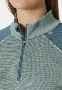 Světle modrý fleecový svetr na zip s texturovanou tkaninou a hladkým panelem. Obsahuje stojáček, polo-zip a jemné logo na rameni.