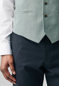 Light green textured vest with three buttons and a pocket, paired with navy trousers and a white shirt, featuring a tailored fit.