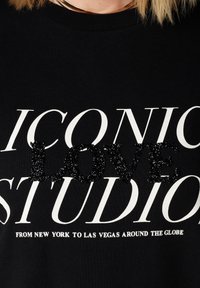 Sweat-shirt noir avec un texte blanc audacieux, "LOVE" en relief noir texturé, et un slogan en dessous évoquant des lieux.