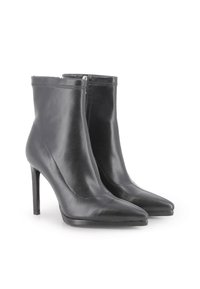 Par de botas de cuero negro hasta el tobillo con puntas afiladas, altos tacones de aguja y cremalleras laterales sobre un fondo blanco.