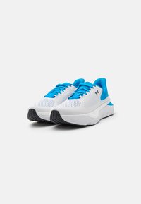 Scarpe sportive bianche con tomaia in mesh, accenti blu e lacci piatti. Suola spessa bianca con battistrada nero texturizzato per una migliore aderenza.