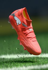 Leuchtend orangefarbener Fußballschuh mit strukturierter Oberfläche, auffälliger Schnürung und silbernem Logo; zeichnet sich durch ein leichtes Design für Agilität auf Gras aus.