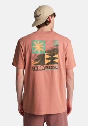 Koraalroze T-shirt met korte mouwen en een grafisch ontwerp met groene en gele blokken en het "BILLA BONG"-logo op de achterkant.